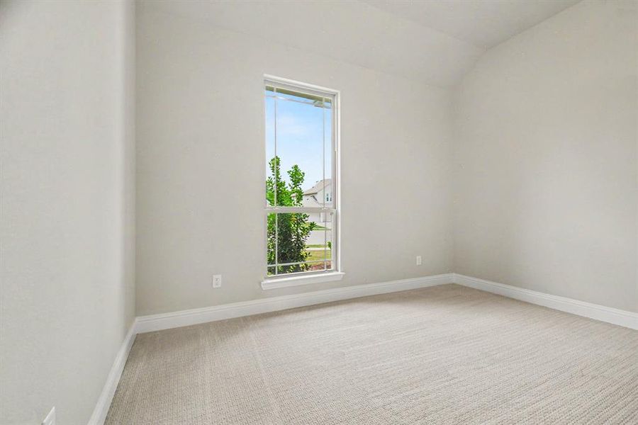 Bright interior room featuring a large window, neutral wall paint, light-toned carpeting, and a vaulted ceiling Bright interior room featuring a large window, neutral wall paint, light-toned carpeting, and a vaulted ceiling