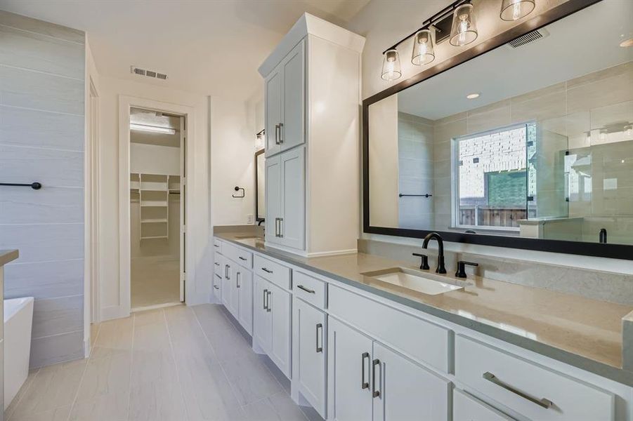Full bathroom featuring double vanity, a walk in closet, a shower stall, and a bathtub