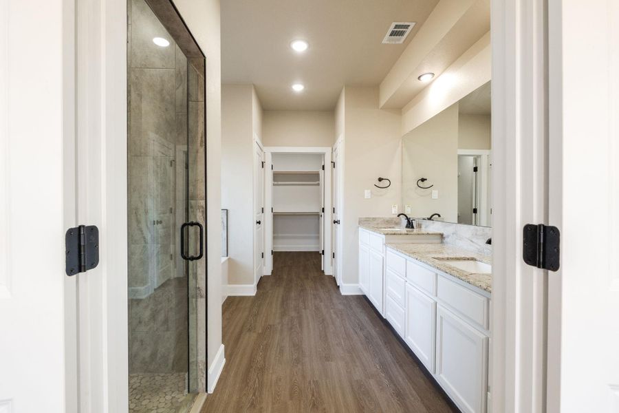 Full bath featuring double vanity, dark wood-style floors, a shower stall, a spacious closet, and recessed lighting