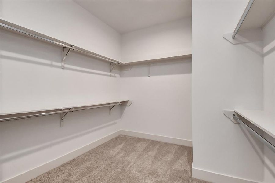 This is a spacious walk-in closet with ample shelving and hanging space, with a neutral color scheme and carpeted flooring. Perfect for organizing clothing and accessories.