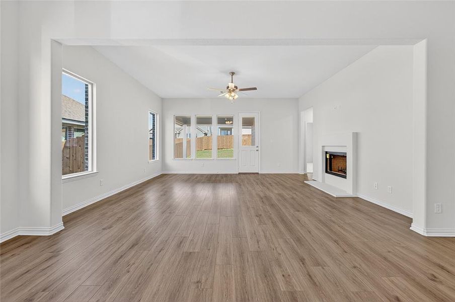 Unfurnished living room with a fireplace with raised hearth, light wood-type flooring, healthy amount of natural light, and a ceiling fan