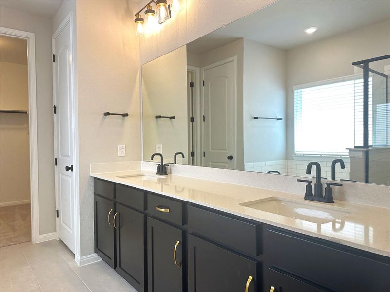 Bathroom featuring double vanity, tile floors, a shower with glass door, a spacious closet, and baseboards Bathroom featuring double vanity, tile floors, a shower with glass door, a spacious closet, and baseboards