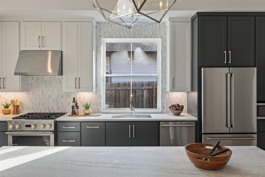 Kitchen featuring sink, ventilation hood, backsplash, light stone counters, and high quality appliances