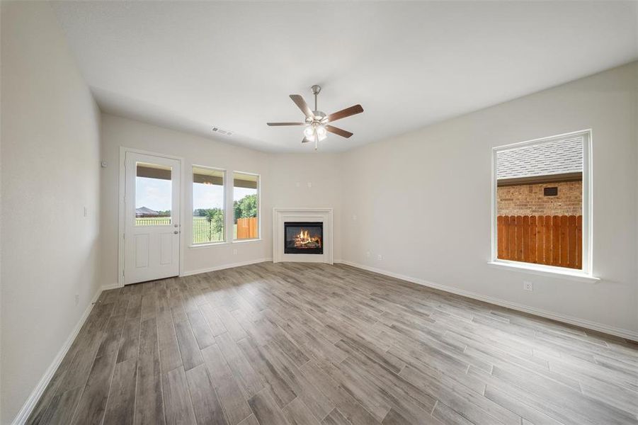 Unfurnished living room with wood finished floors, a ceiling fan, and a glass covered fireplace