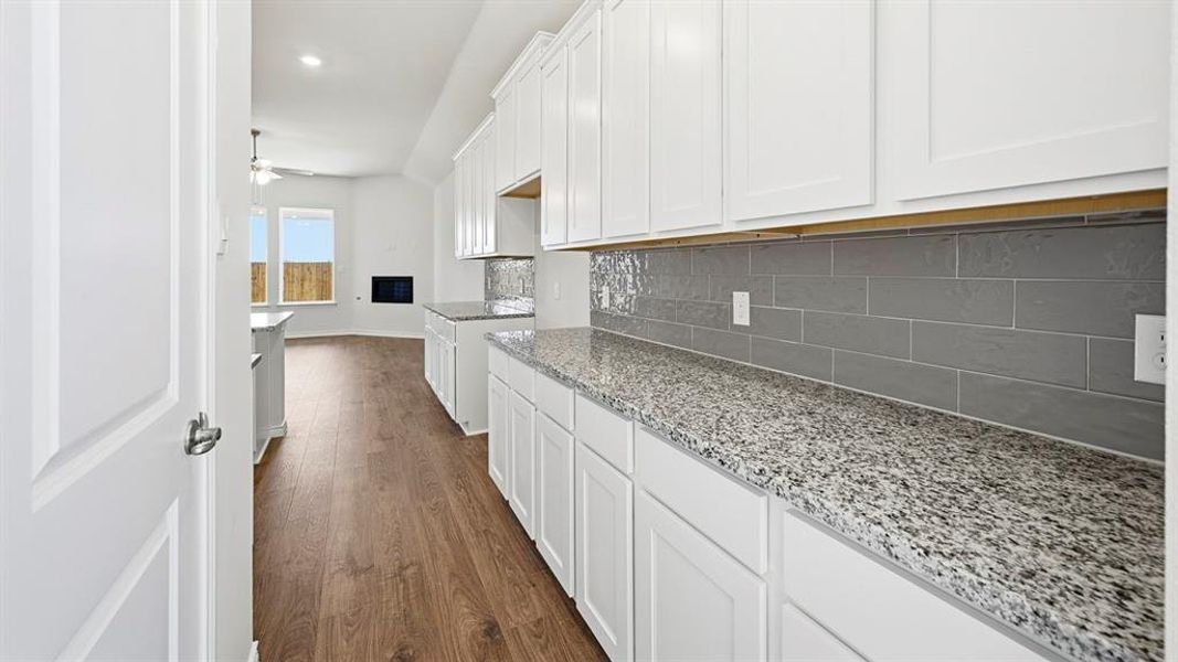 Kitchen with white cabinets, dark wood-style floors, light stone countertops, ceiling fan, and tasteful backsplash