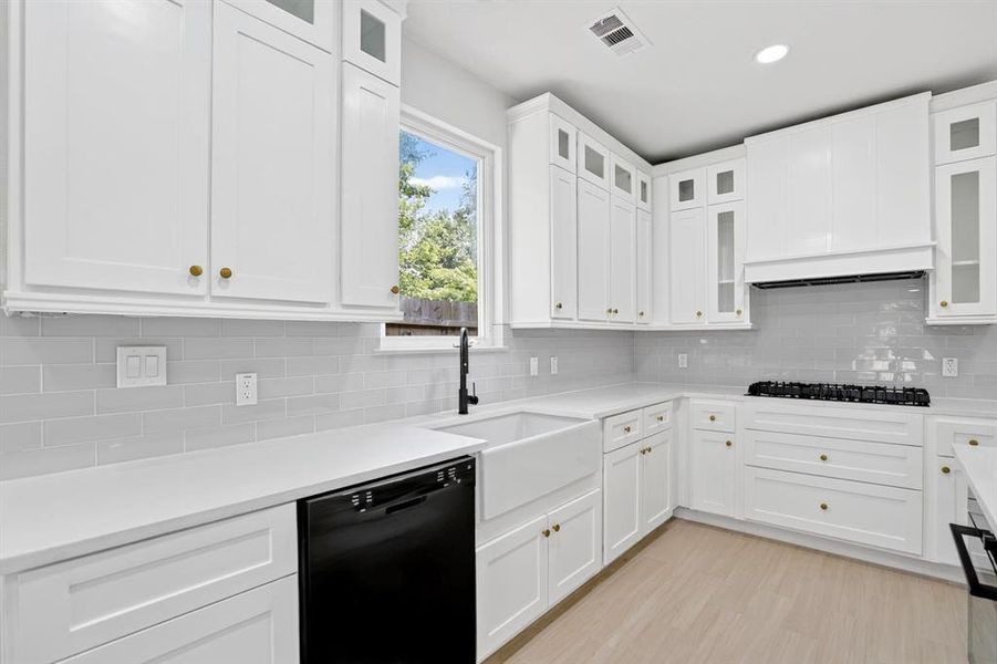Contemporary kitchen featuring white shaker cabinetry, light wood-finish flooring, a farmhouse sink with a matte black faucet, light grey subway tile backsplash, and white countertops