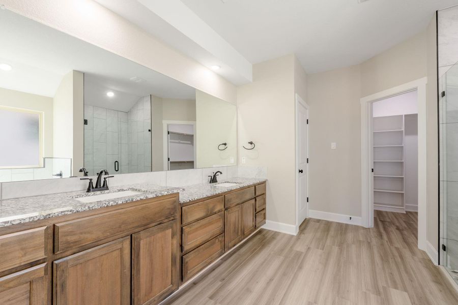 Full bath with a walk in closet, a shower stall, double vanity, and light wood finished floors
