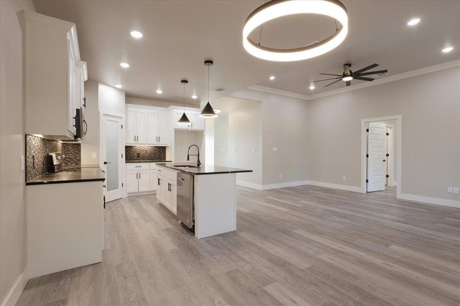 Kitchen featuring sink, light hardwood / wood-style floors, decorative light fixtures, white cabinets, and a center island with sink