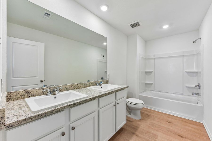 Bathroom featuring a dual vanity with a granite-style countertop, white cabinetry, and undermount sinks