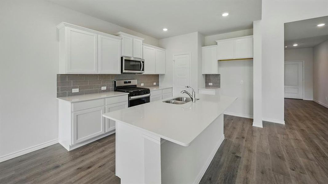 Modern kitchen featuring a central island with a double basin sink, white cabinetry with crown molding, stainless steel appliances, and a gray subway tile backsplash Modern kitchen featuring a central island with a double basin sink, white cabinetry with crown molding, stainless steel appliances, and a gray subway tile backsplash