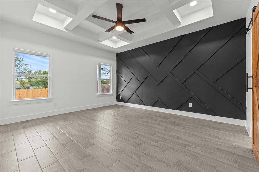 Empty room featuring coffered ceiling, a wealth of natural light, light wood-type flooring, and a barn door