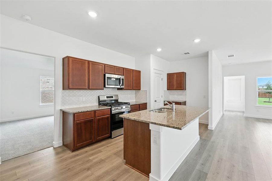 Kitchen with decorative backsplash, stainless steel appliances, light stone counters, a kitchen island with sink, and light wood-style floors Kitchen with decorative backsplash, stainless steel appliances, light stone counters, a kitchen island with sink, and light wood-style floors