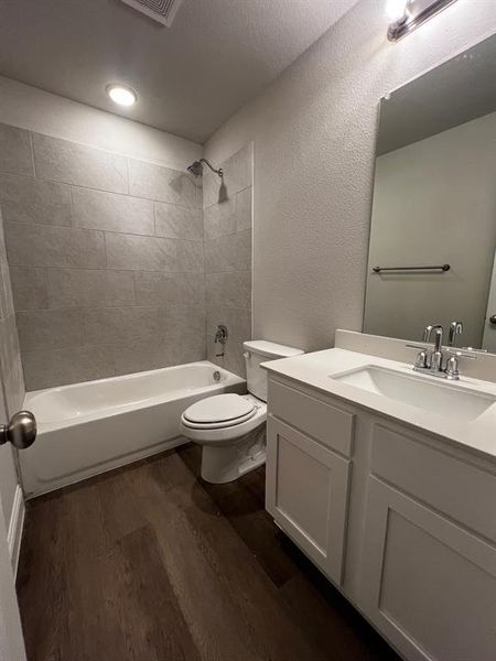 Full bathroom with vanity, toilet, tiled shower / bath combo, a textured ceiling, and hardwood / wood-style floors