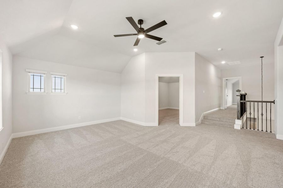Spacious bonus room with vaulted ceiling, ceiling fan, carpet flooring, and staircase landing nearby Spacious bonus room with vaulted ceiling, ceiling fan, carpet flooring, and staircase landing nearby