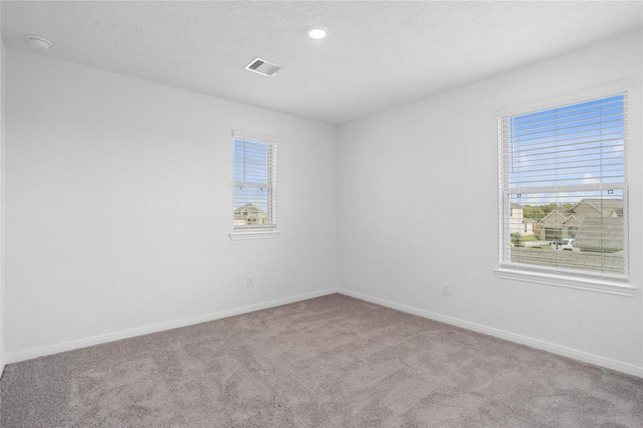 This secondary bedroom offers comfort and style with plush carpeting, neutral paint tones, recessed lighting, large windows with blinds, and a generously sized closet.