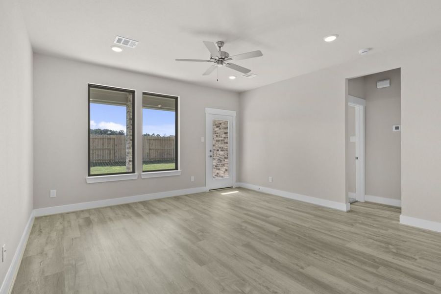 Image of a living room with beige walls, two windows, light brown flooring, and a ceiling fan