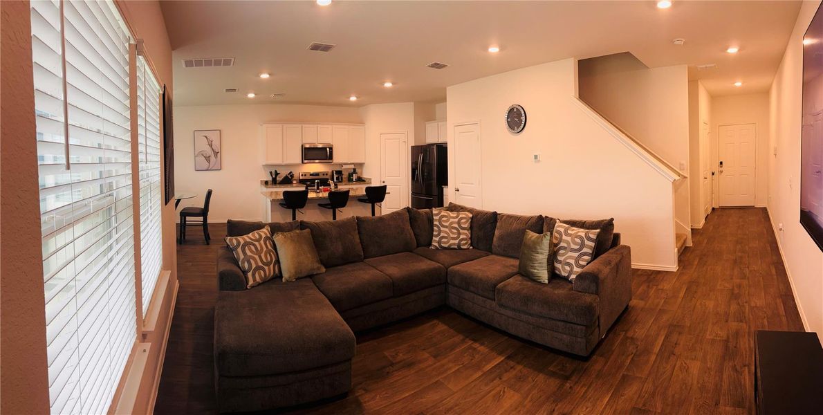 Open-concept living area featuring wood-finish flooring, recessed lighting, and a kitchen with white cabinetry and stainless steel appliances Open-concept living area featuring wood-finish flooring, recessed lighting, and a kitchen with white cabinetry and stainless steel appliances