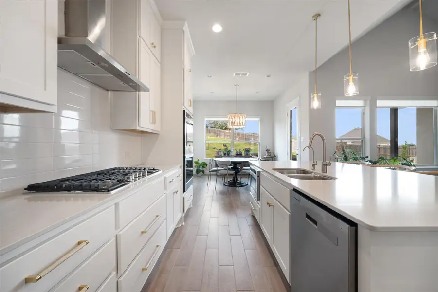Kitchen featuring stainless steel appliances, light countertops, wall chimney exhaust hood, dark wood-type flooring, and a center island with sink