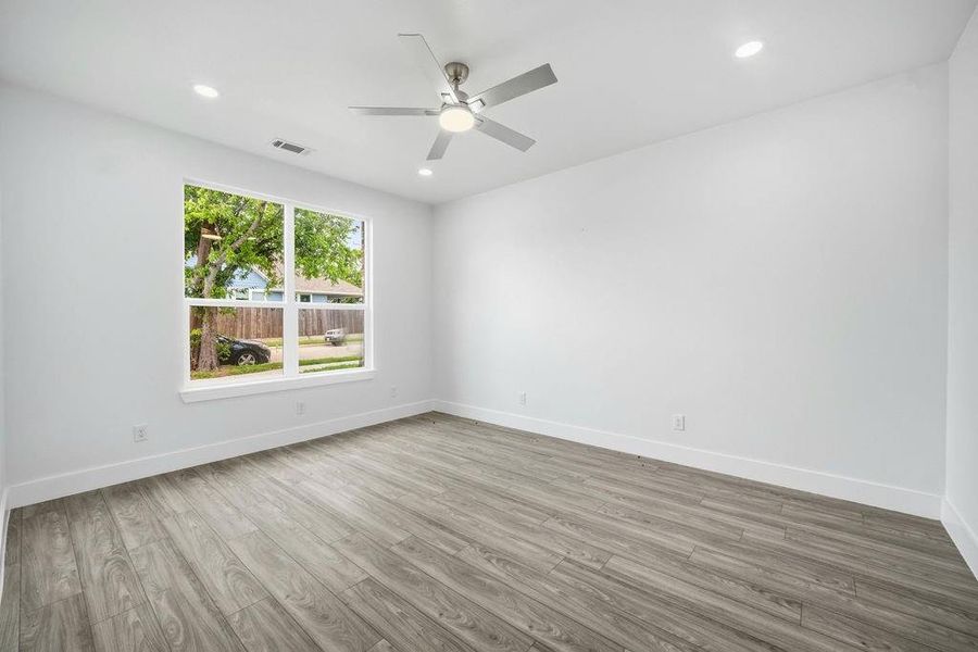 Bright room featuring wood-finish flooring, a large window with white trim, a ceiling fan with integrated lighting, and recessed ceiling lights Bright room featuring wood-finish flooring, a large window with white trim, a ceiling fan with integrated lighting, and recessed ceiling lights