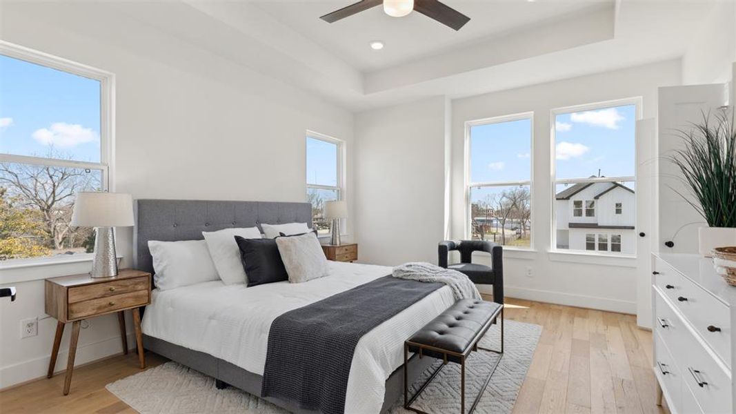 Bright and spacious bedroom with large windows, neutral tones, and hardwood floors. Features a stylish bed, ceiling fan, and modern furnishings, offering a cozy and inviting atmosphere.