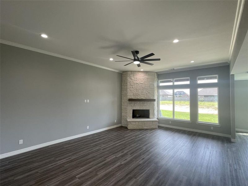 Unfurnished living room featuring crown molding, dark wood-type flooring, a fireplace, a ceiling fan, and recessed lighting