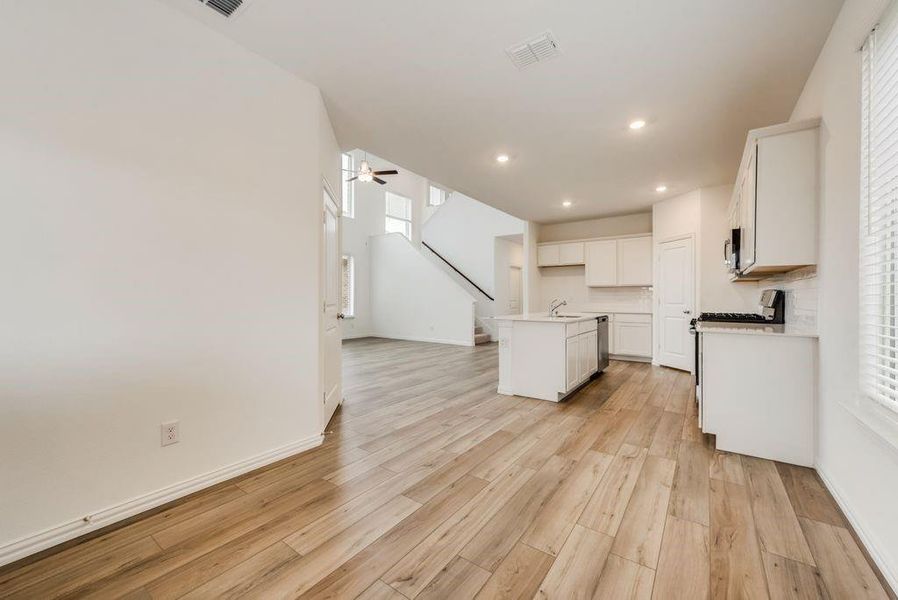 Kitchen with light wood-type flooring, white cabinets, a kitchen island with sink, and ceiling fan