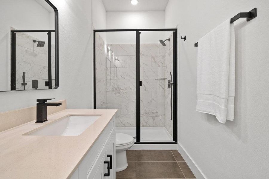 Full bath with a marble finish shower, vanity, and dark tile patterned flooring