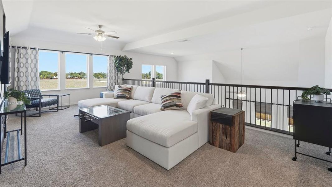 Spacious loft area featuring carpet flooring, a ceiling fan with light fixture, multiple windows, and a black metal railing overlooking the lower level Spacious loft area featuring carpet flooring, a ceiling fan with light fixture, multiple windows, and a black metal railing overlooking the lower level