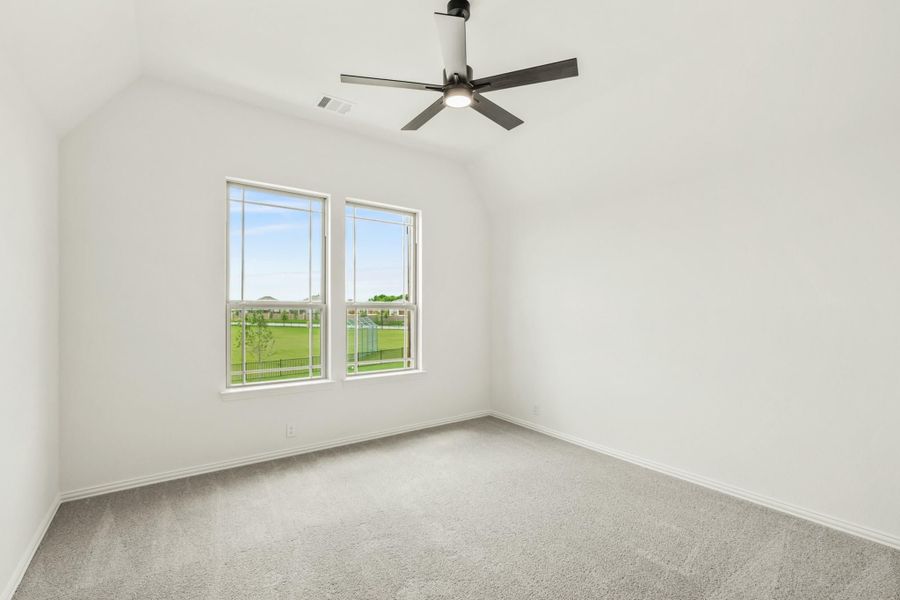 Empty bedroom with vaulted ceiling, ceiling fan, carpet flooring, and two windows overlooking a green yard Empty bedroom with vaulted ceiling, ceiling fan, carpet flooring, and two windows overlooking a green yard