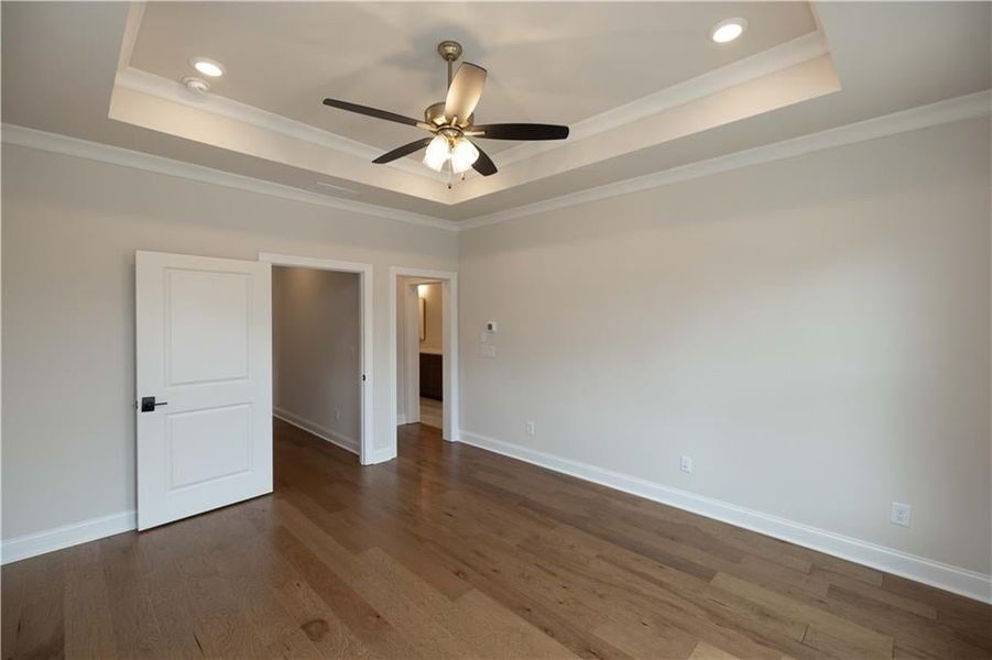 Empty room featuring ceiling fan, ornamental molding, a tray ceiling, and dark hardwood / wood-style flooring