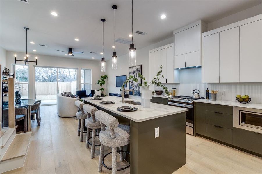 Kitchen featuring white cabinetry, decorative light fixtures, appliances with stainless steel finishes, an island with sink, and light hardwood / wood-style floors