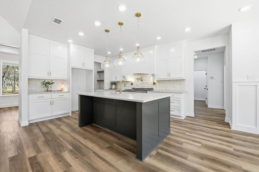 Kitchen with an island with sink, two tone cabinetry, dark wood-style flooring, decorative backsplash, and hanging light fixtures