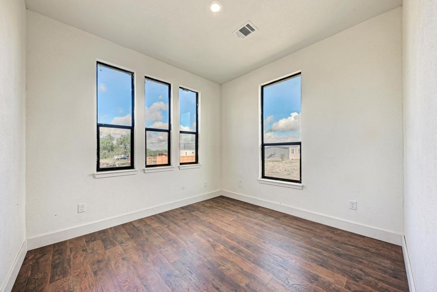 Rich wood-look flooring and dark-trimmed windows define this versatile, light-filled room.