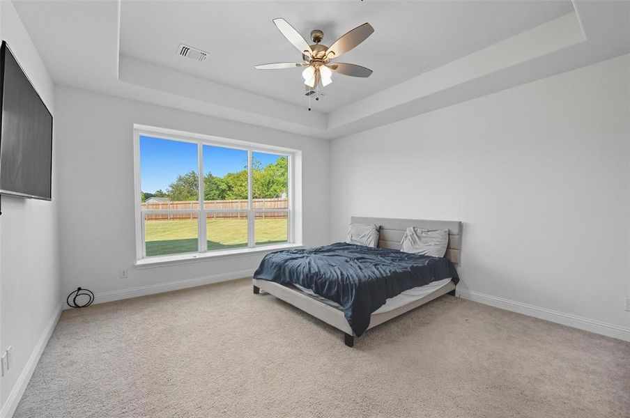 Bedroom with a tray ceiling, light colored carpet, and a ceiling fan