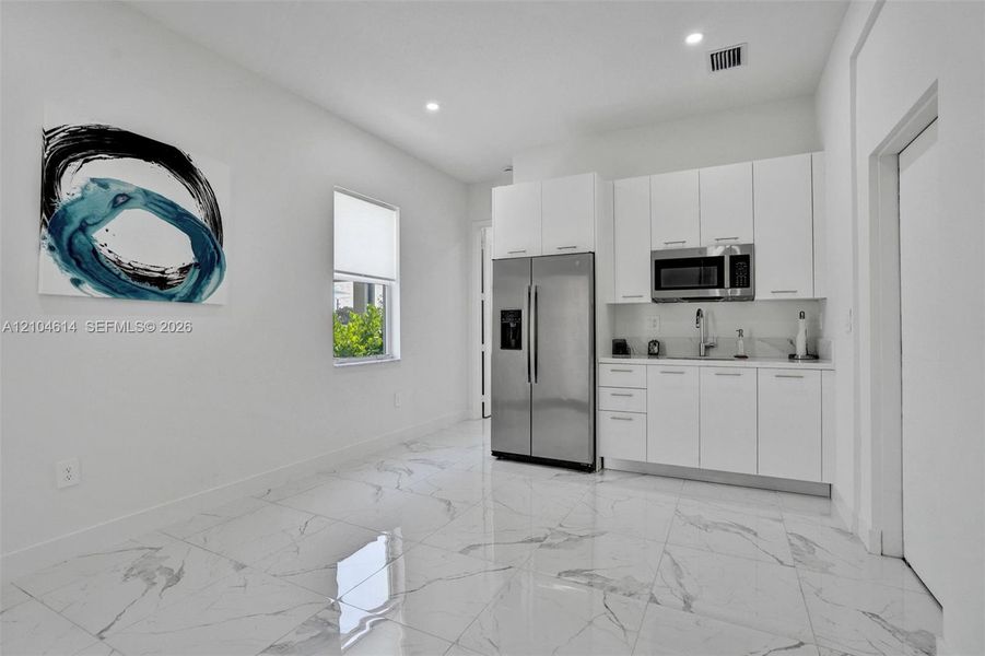 White shaker-style cabinetry with stainless steel hardware, stainless steel side-by-side refrigerator, stainless steel microwave, and polished tile flooring