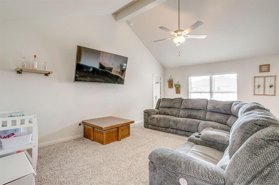 Carpeted living area featuring beam ceiling, high vaulted ceiling, and ceiling fan