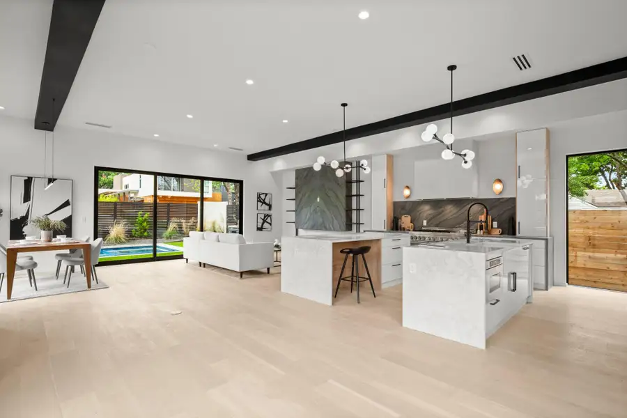 Kitchen featuring beam ceiling, light stone counters, open floor plan, a chandelier, and modern cabinets