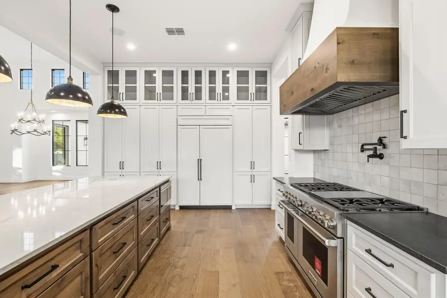 Kitchen featuring dual tone cabinetry, dark stone counters, premium appliances, glass insert cabinets, and light wood-style floors
