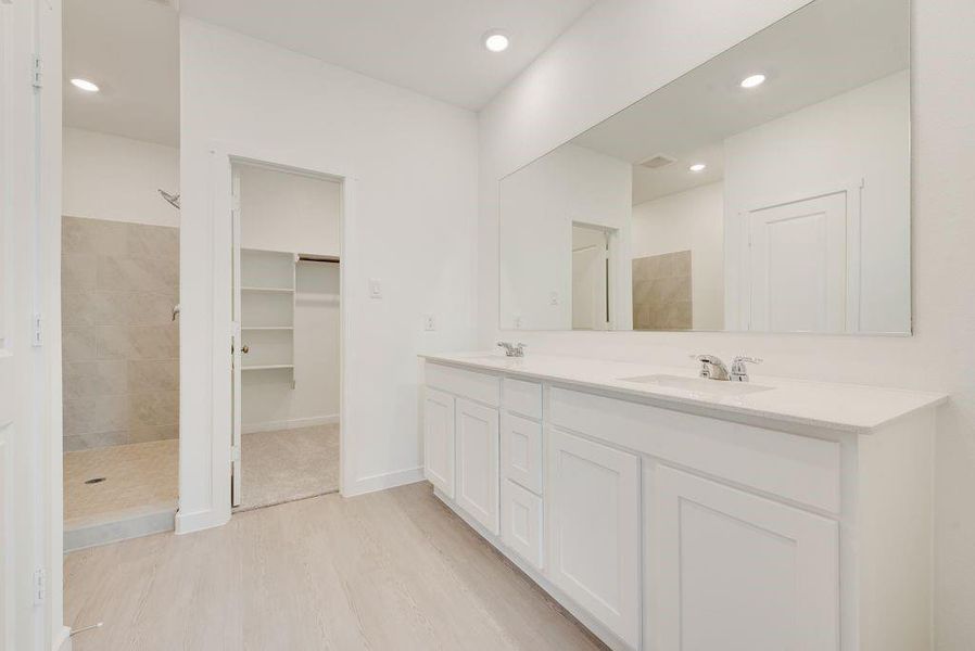 Bathroom featuring double vanity, wood finished floors, a tile shower, recessed lighting, and a spacious closet