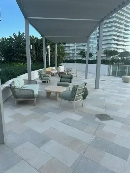 Outdoor terrace featuring light-toned stone tile flooring, a metal pergola, low-profile perimeter walls, and built-in wall-mounted lighting Outdoor terrace featuring light-toned stone tile flooring, a metal pergola, low-profile perimeter walls, and built-in wall-mounted lighting