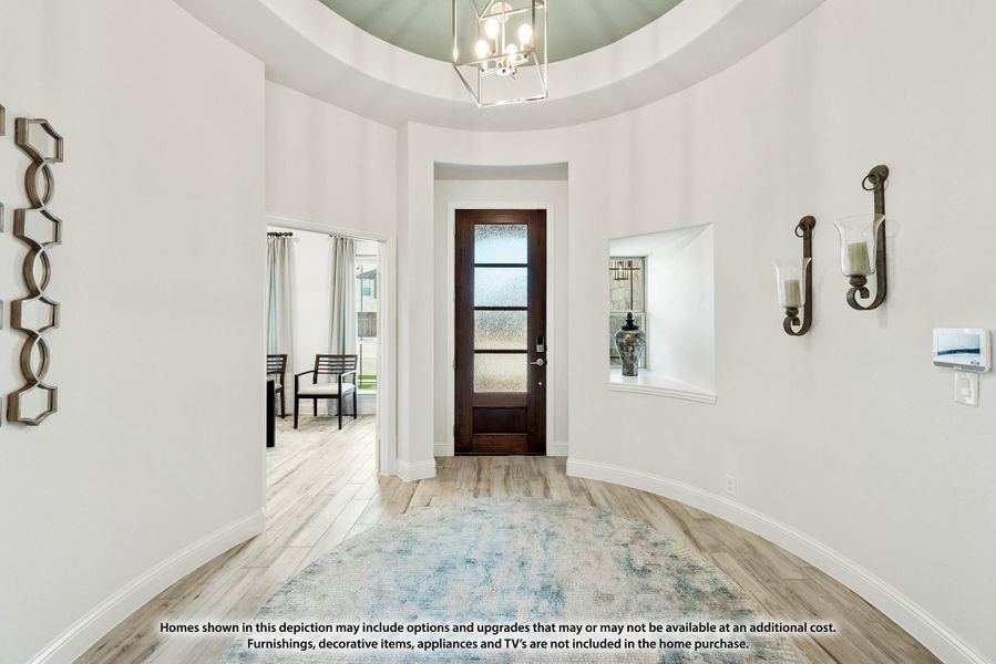 Rounded foyer with tray ceiling, chandelier, dark wood front door, and light hardwood floors Rounded foyer with tray ceiling, chandelier, dark wood front door, and light hardwood floors