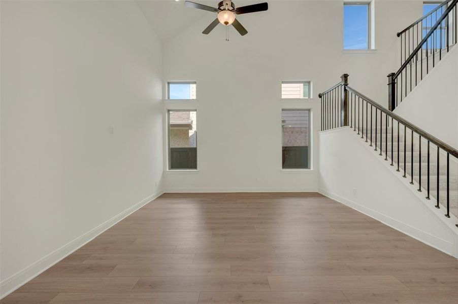 Two-story living area featuring vaulted ceilings, wood-finish flooring, a contemporary ceiling fan, and a staircase with dark wrought iron balusters Two-story living area featuring vaulted ceilings, wood-finish flooring, a contemporary ceiling fan, and a staircase with dark wrought iron balusters