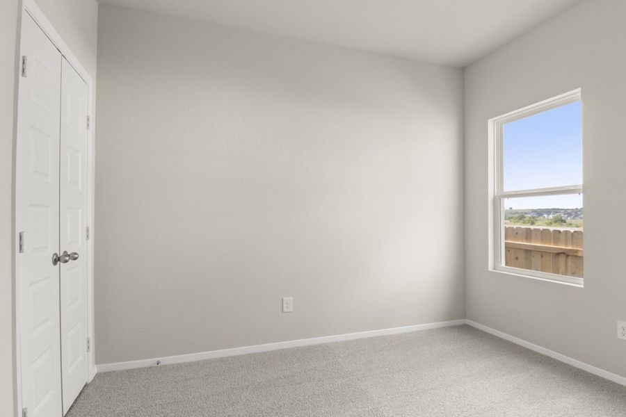 Image of a bedroom with light grey walls, tan carpeting and a window