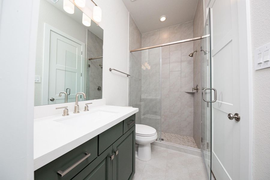 This en-suite bathroom offers stained cabinet topped with quartz countertop and undermount sink, brushed nickel fixtures, and a large walk-in shower with tile surround. This en-suite bathroom offers stained cabinet topped with quartz countertop and undermount sink, brushed nickel fixtures, and a large walk-in shower with tile surround.