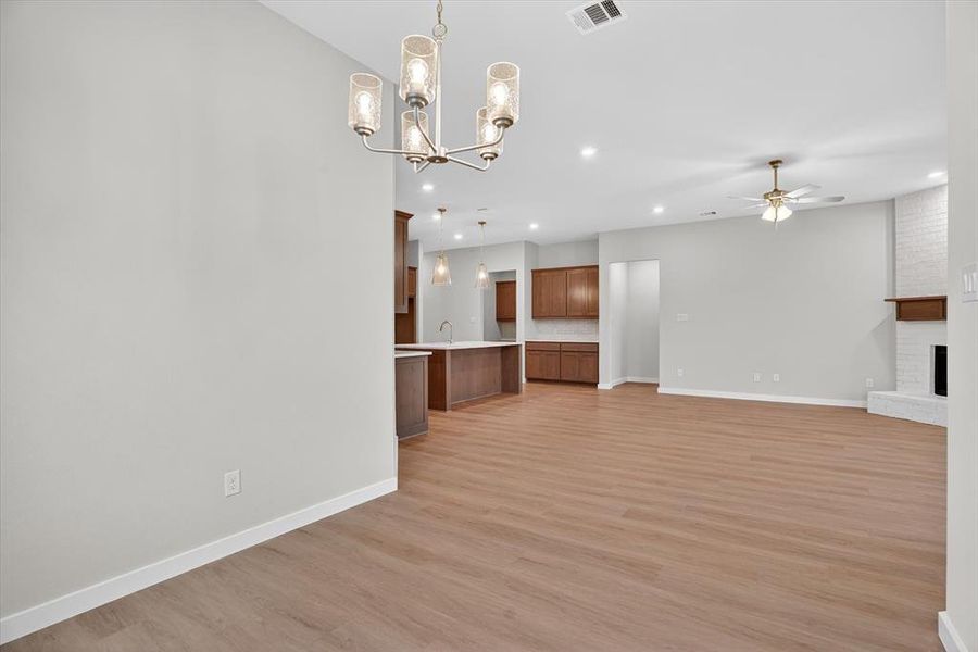 Open-concept living space featuring wood-finish flooring, a contemporary chandelier, recessed lighting, and a white brick fireplace with a wood mantle
