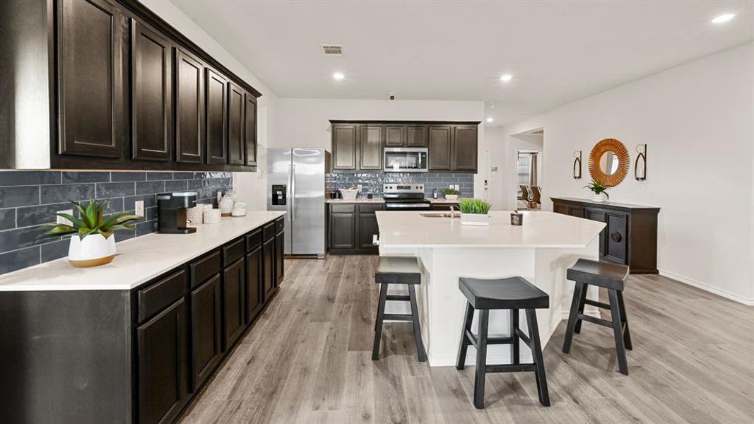 The kitchen features dark wood cabinetry, stainless steel appliances, a white island with seating, and light-colored flooring