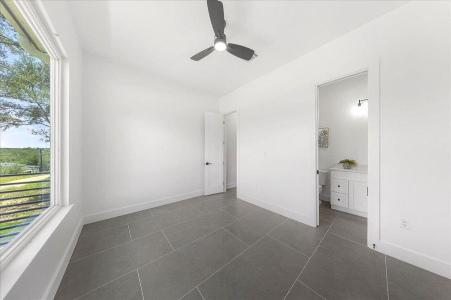 Unfurnished bedroom featuring multiple windows, dark tile patterned floors, connected bathroom, and a ceiling fan Unfurnished bedroom featuring multiple windows, dark tile patterned floors, connected bathroom, and a ceiling fan