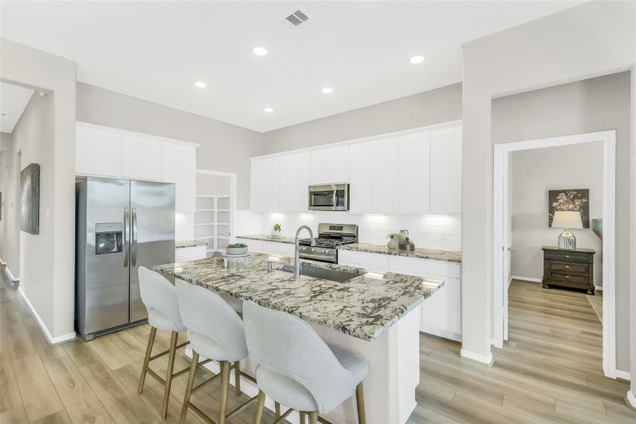 Gourmet kitchen featuring a large granite island with seating, designer cabinetry, and stainless steel appliances.