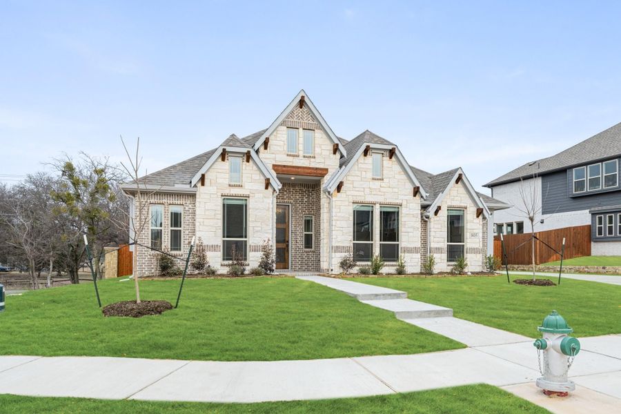 Single-story home with stone and brick exterior, pitched roof, large windows, and green front lawn with walkway. Single-story home with stone and brick exterior, pitched roof, large windows, and green front lawn with walkway.
