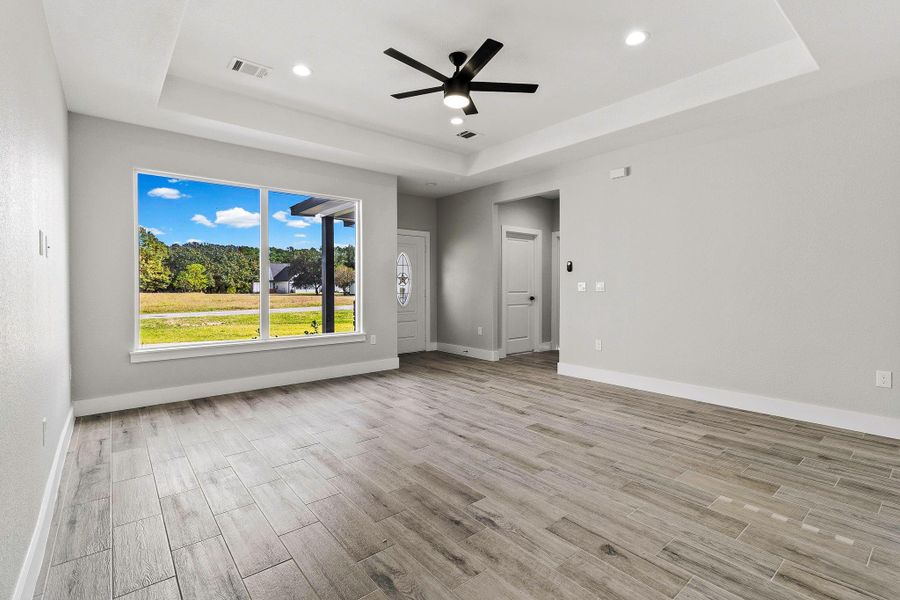 Bright and modern living space with large windows offering scenic views, featuring wood-look tile flooring, recessed lighting, and a stylish ceiling fan.